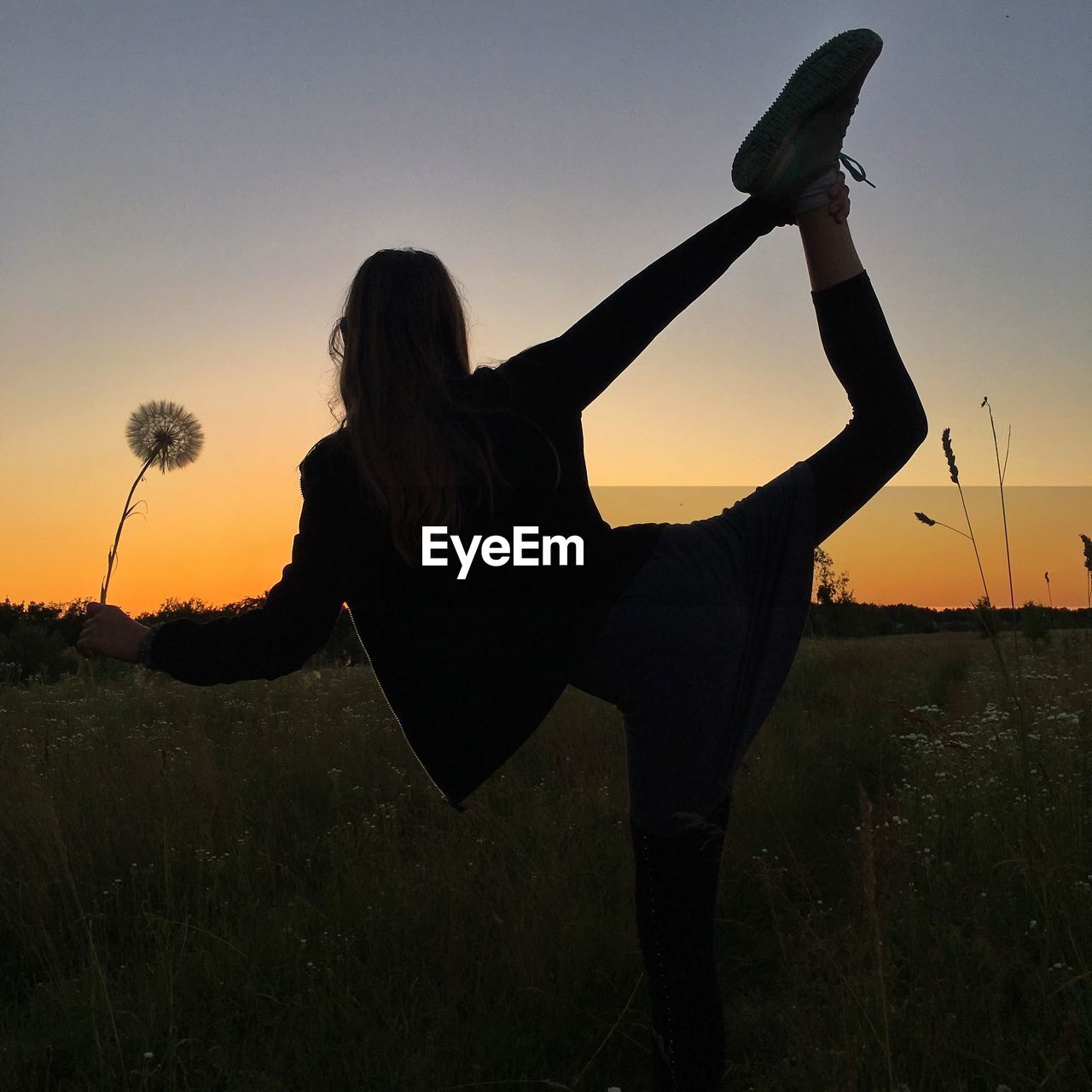 Silhouette woman standing on one leg against sky during sunset