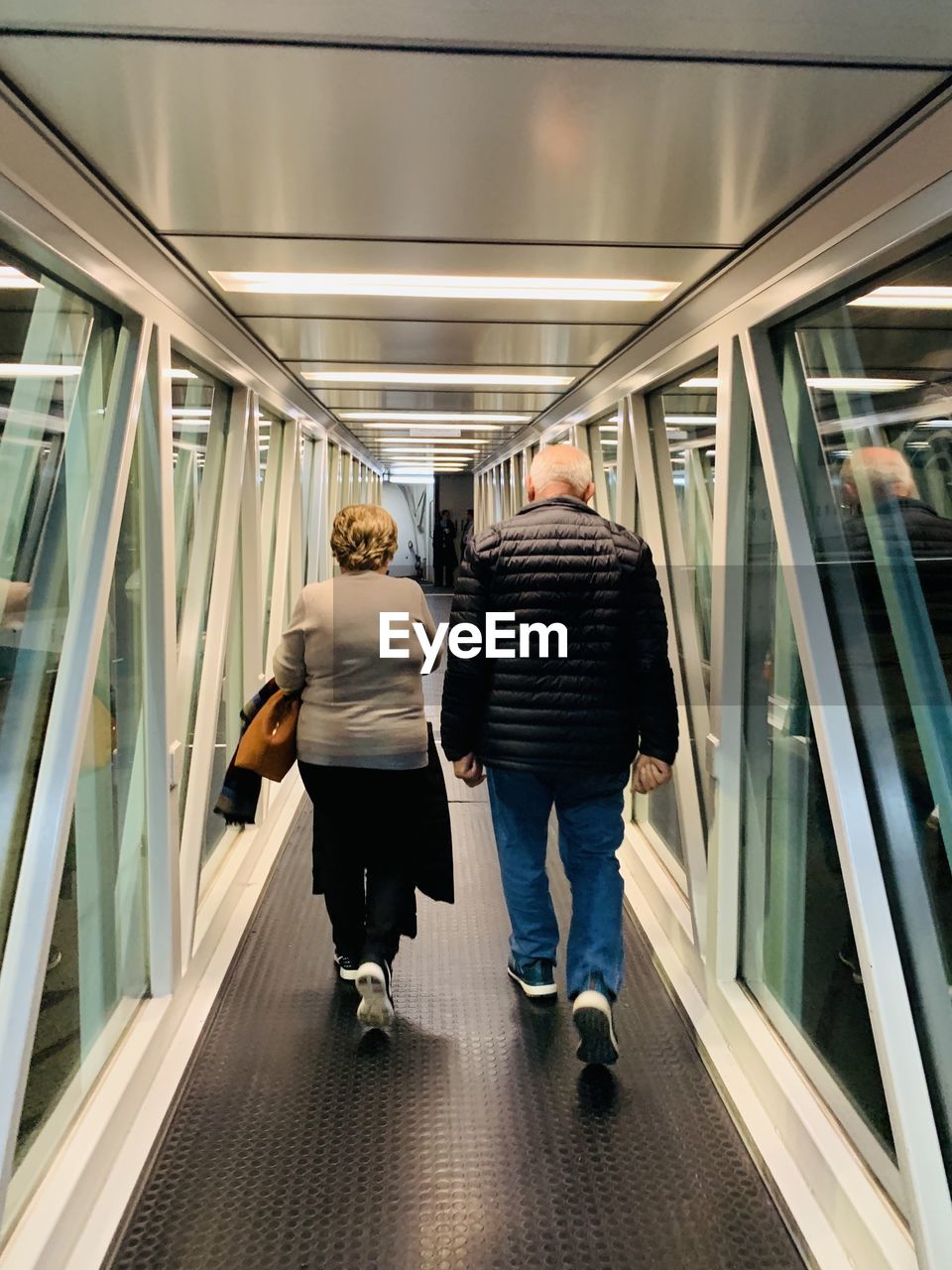 Rear view of senior couple walking on passenger boarding bridge