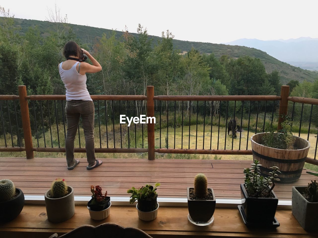 REAR VIEW OF WOMAN STANDING BY RAILING AGAINST MOUNTAIN