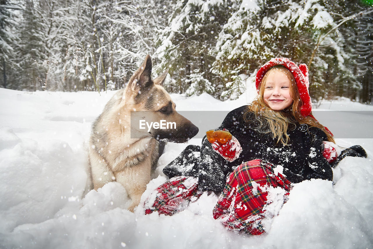 portrait of smiling young woman with dog on snow covered field