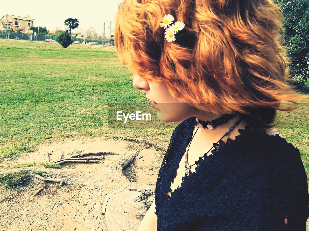 Side view of young woman wearing white daisies while sitting at park