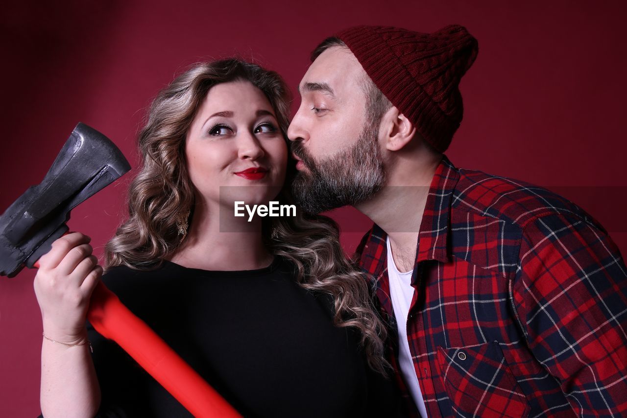 Man kissing girlfriend holding axe by red wall