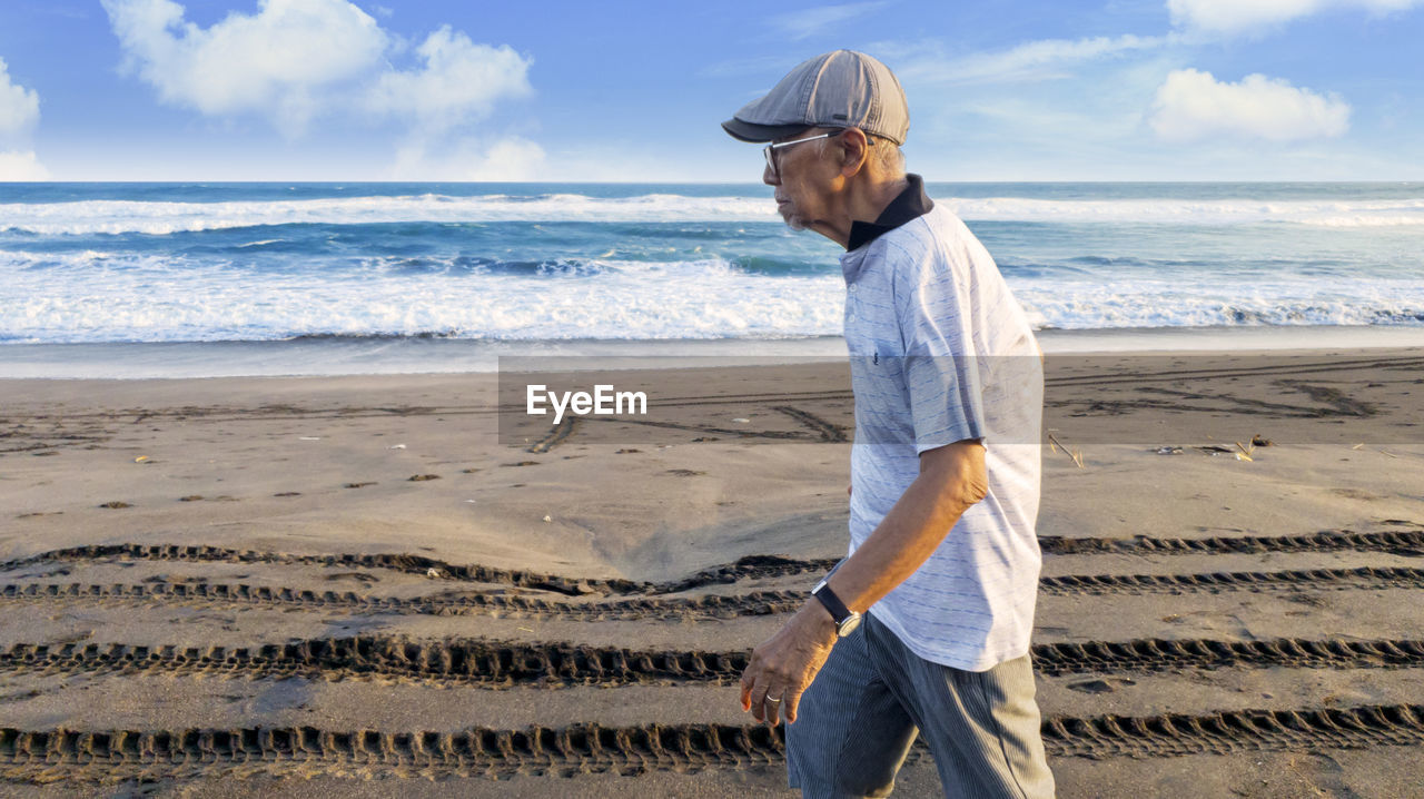 MAN STANDING ON BEACH AGAINST SEA