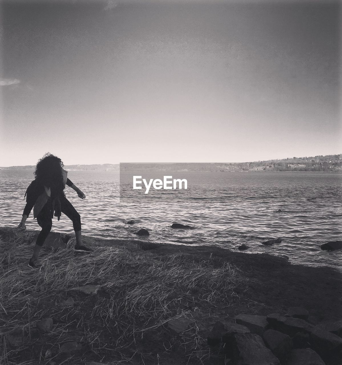 Woman throwing stone in sea against sky