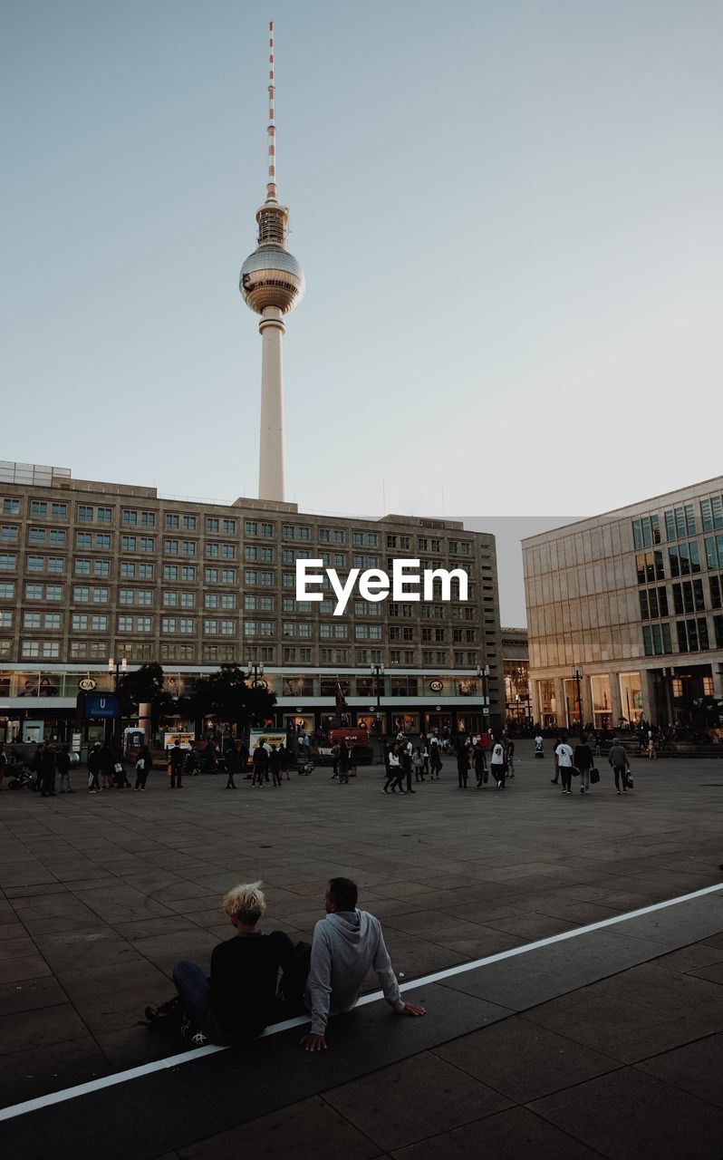 People at alexanderplatz with fernsehturm against sky in city