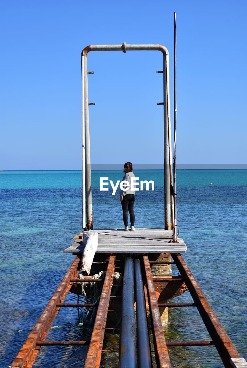 Rear view of woman standing on pier over sea against clear blue sky