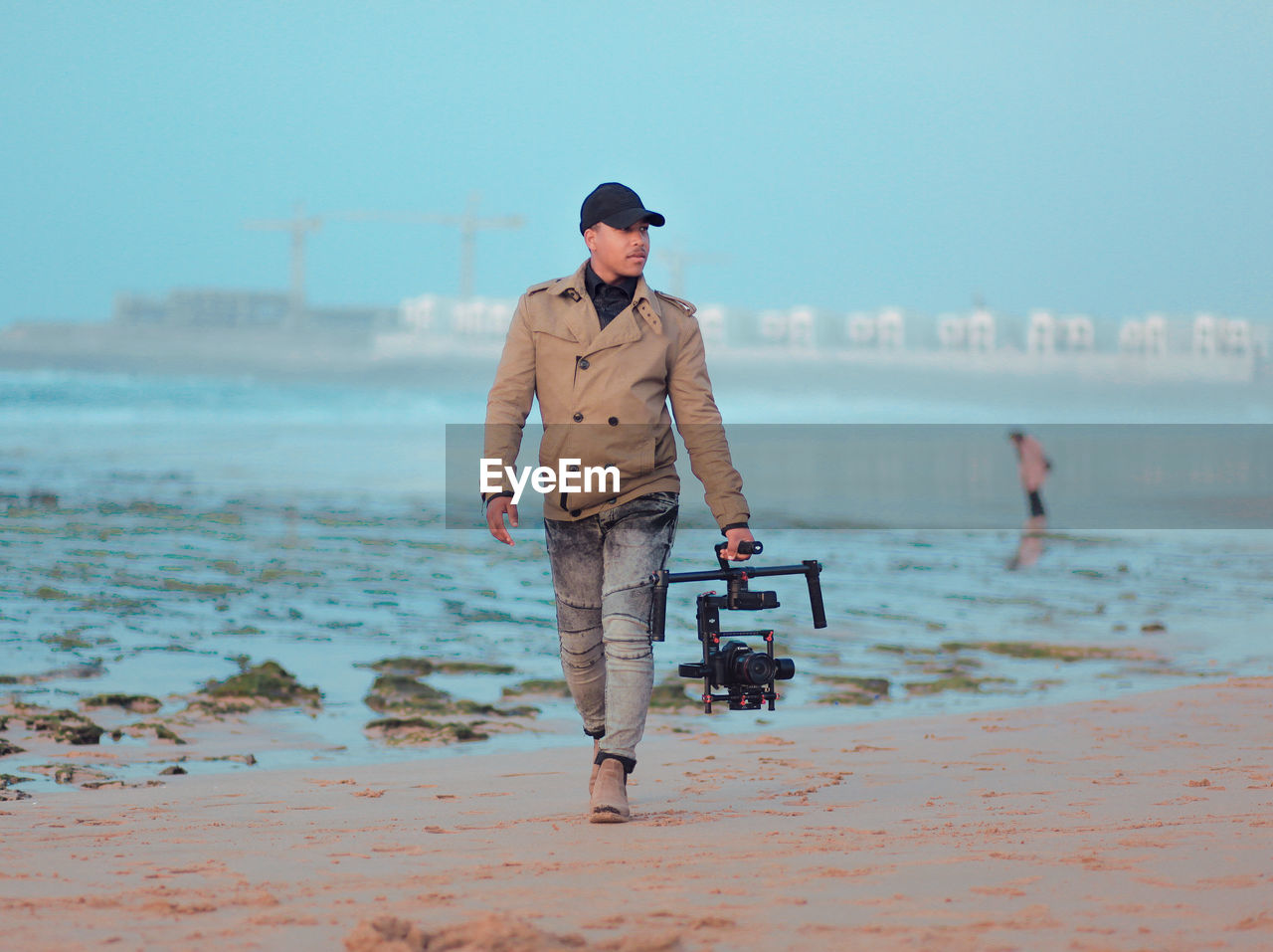 Full length of man holding camera while walking at beach