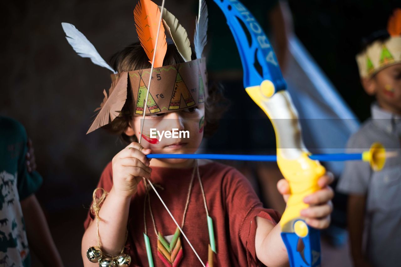 Cute boy wearing colorful artificial feathers playing archery