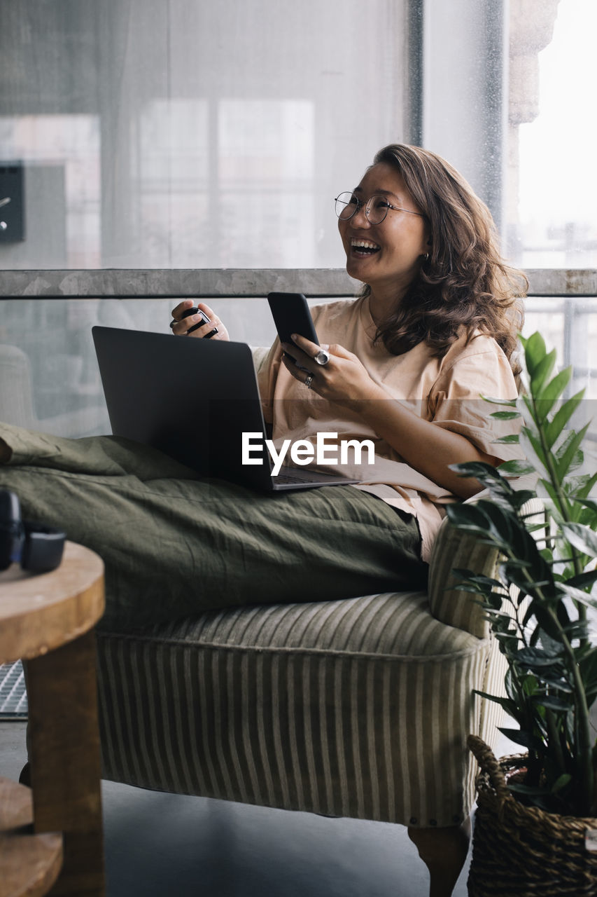 Female computer programmer with laptop and smart phone laughing in office
