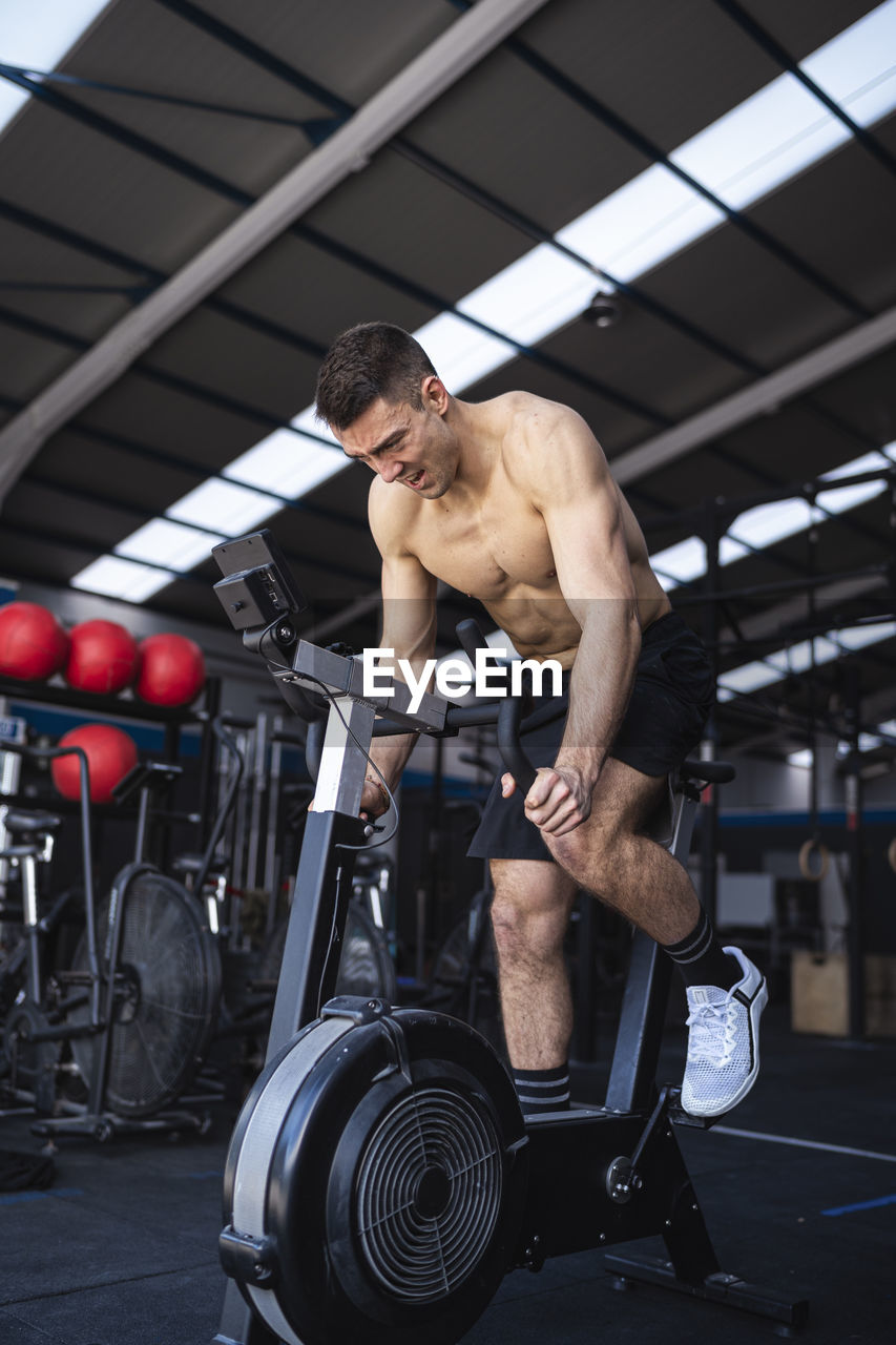 Motivated male athlete exercising on exercise bike in gym