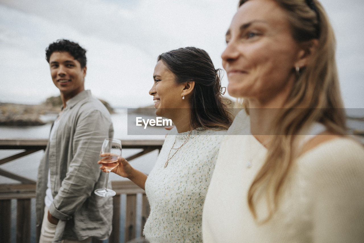 Happy woman holding wine while walking with friends on bridge