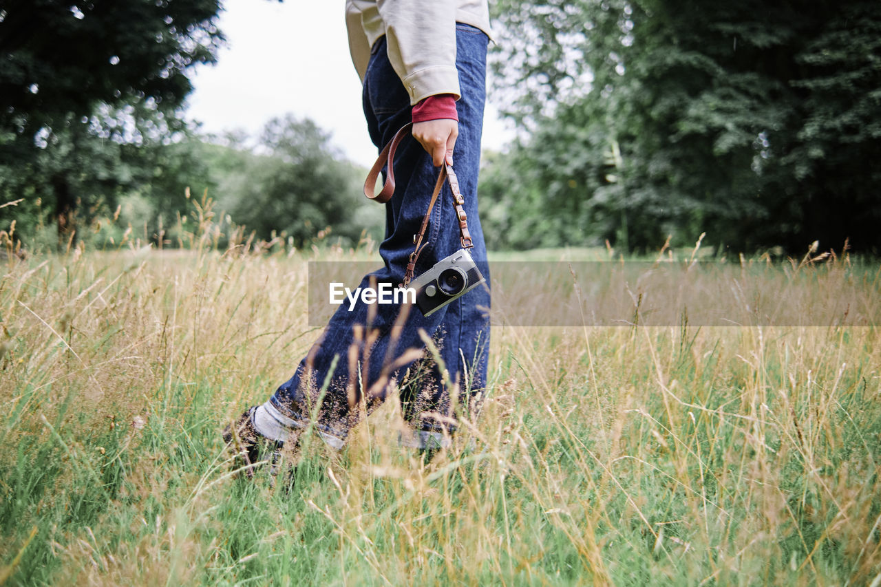 Woman holding camera while walking on grass in public park