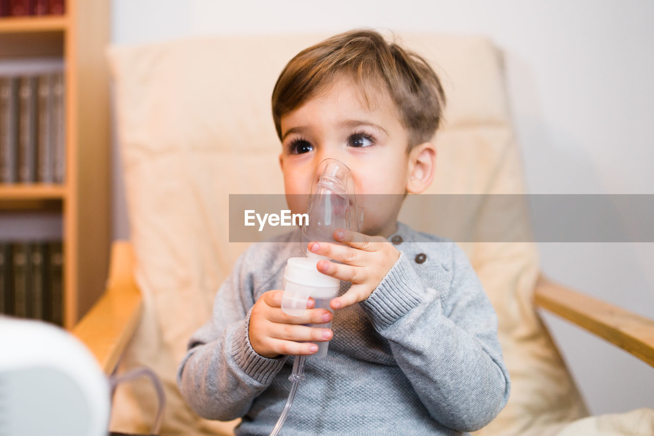 Boy looking away while inhaling through respiratory mask at home