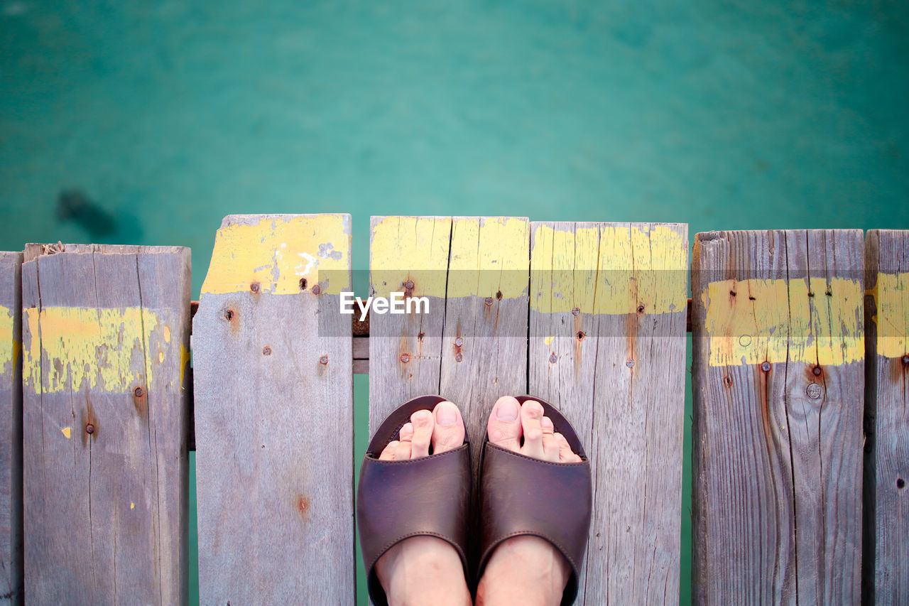 LOW SECTION OF WOMAN STANDING ON WOODEN PIER AGAINST SKY