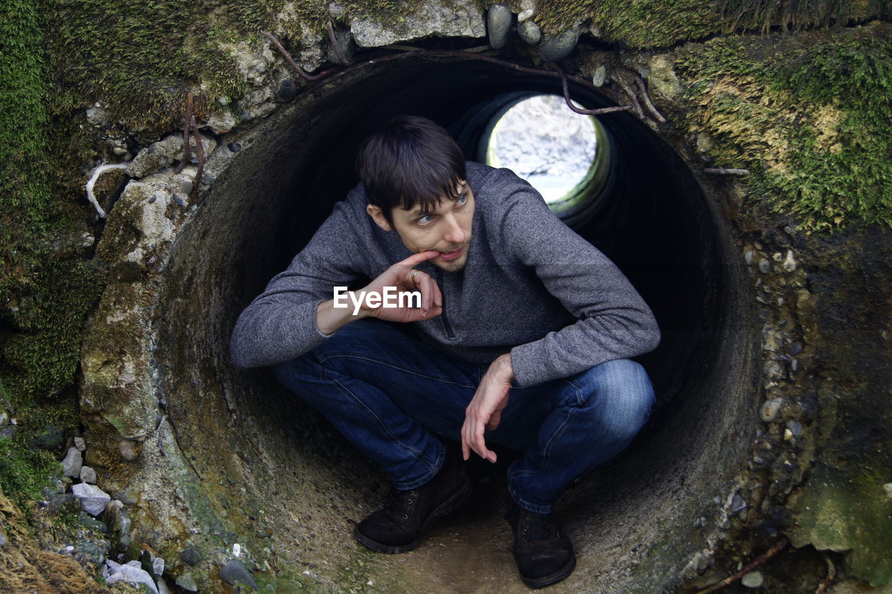 Mid adult man crouching in cement pipe