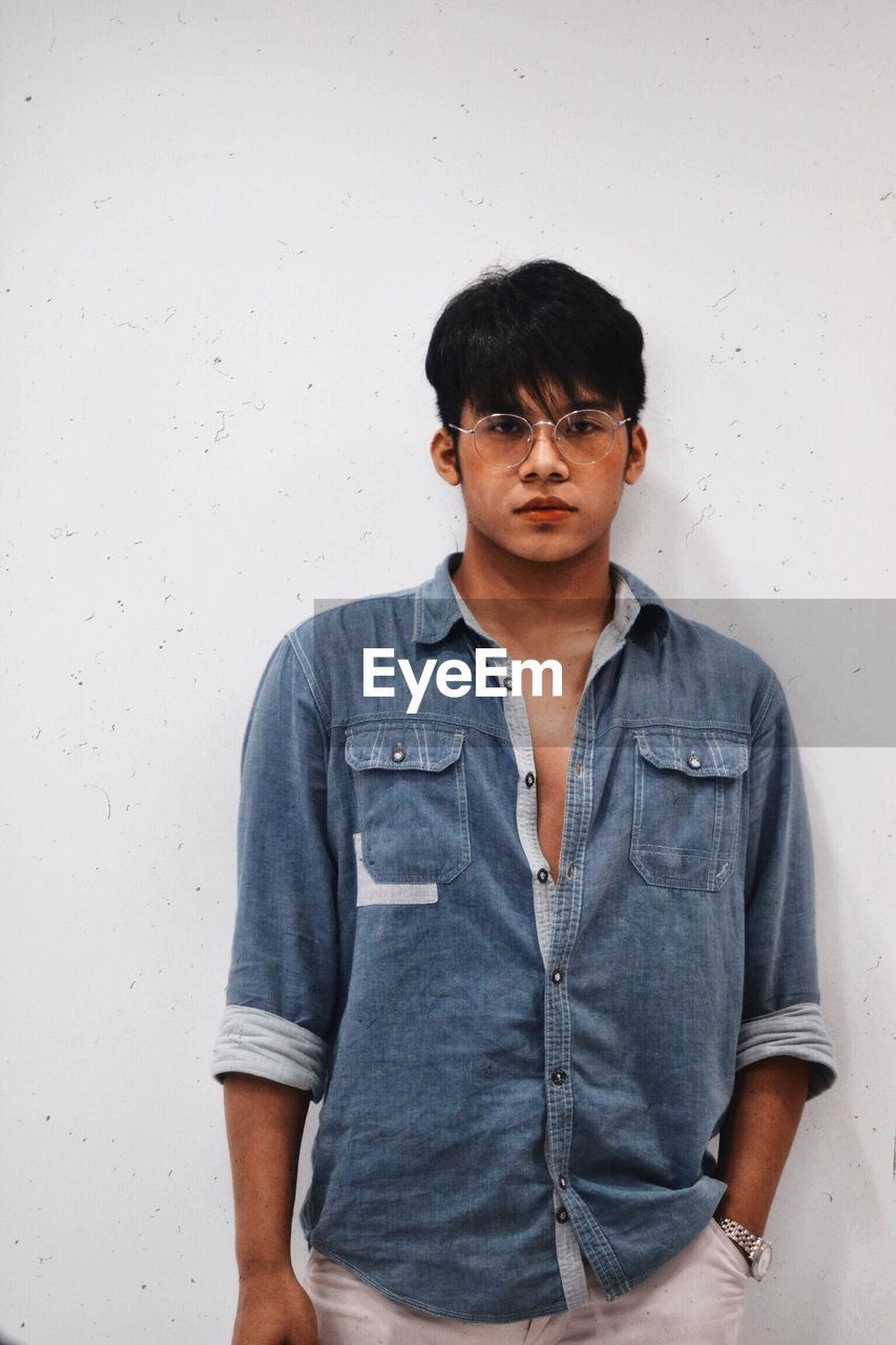 Portrait of serious young man standing against wall