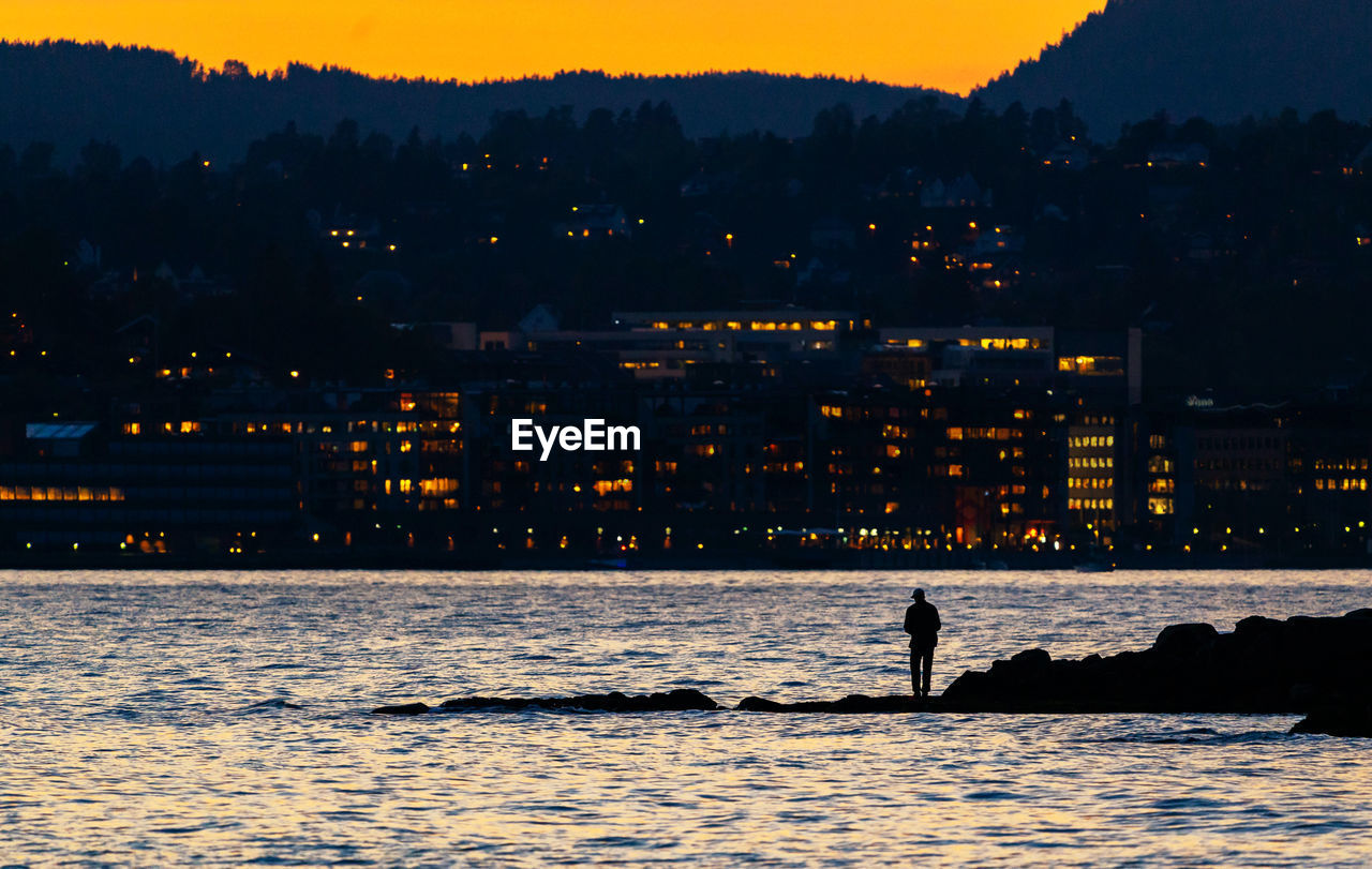 Rear view of silhouette man by sea during sunset