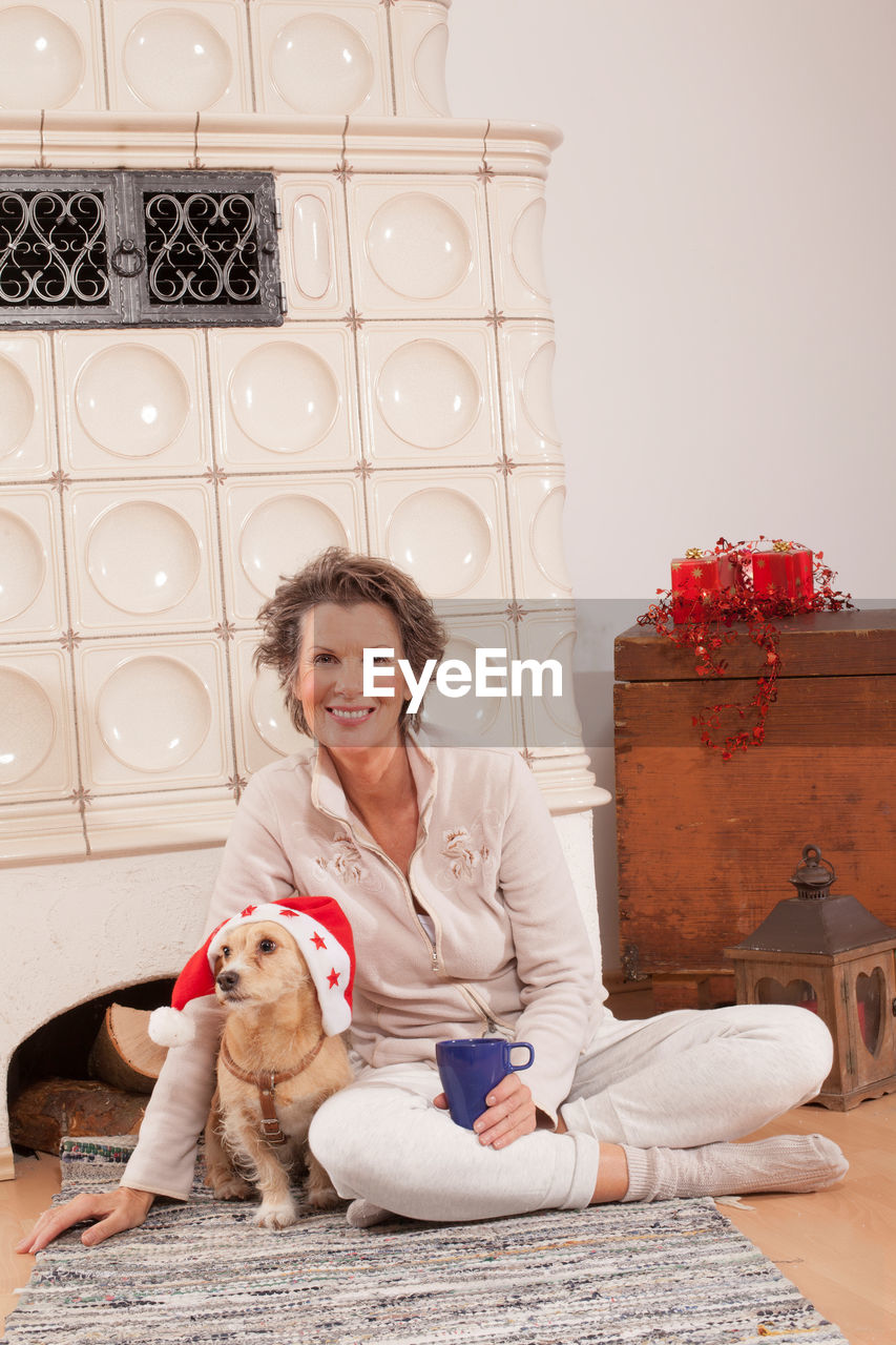 Portrait of woman with dog sitting by fireplace at home during christmas