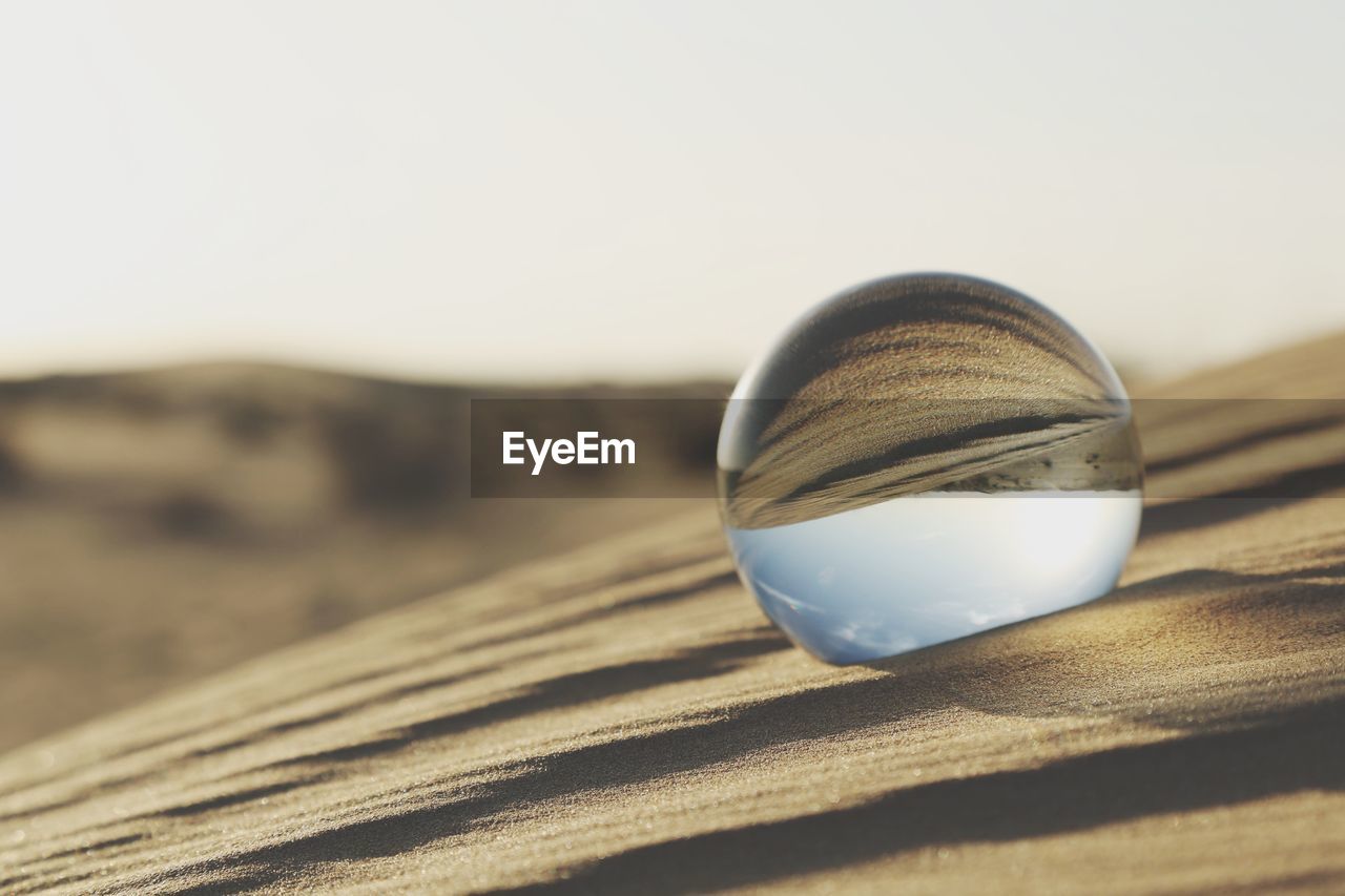 Close-up of crystal ball on beach against clear sky