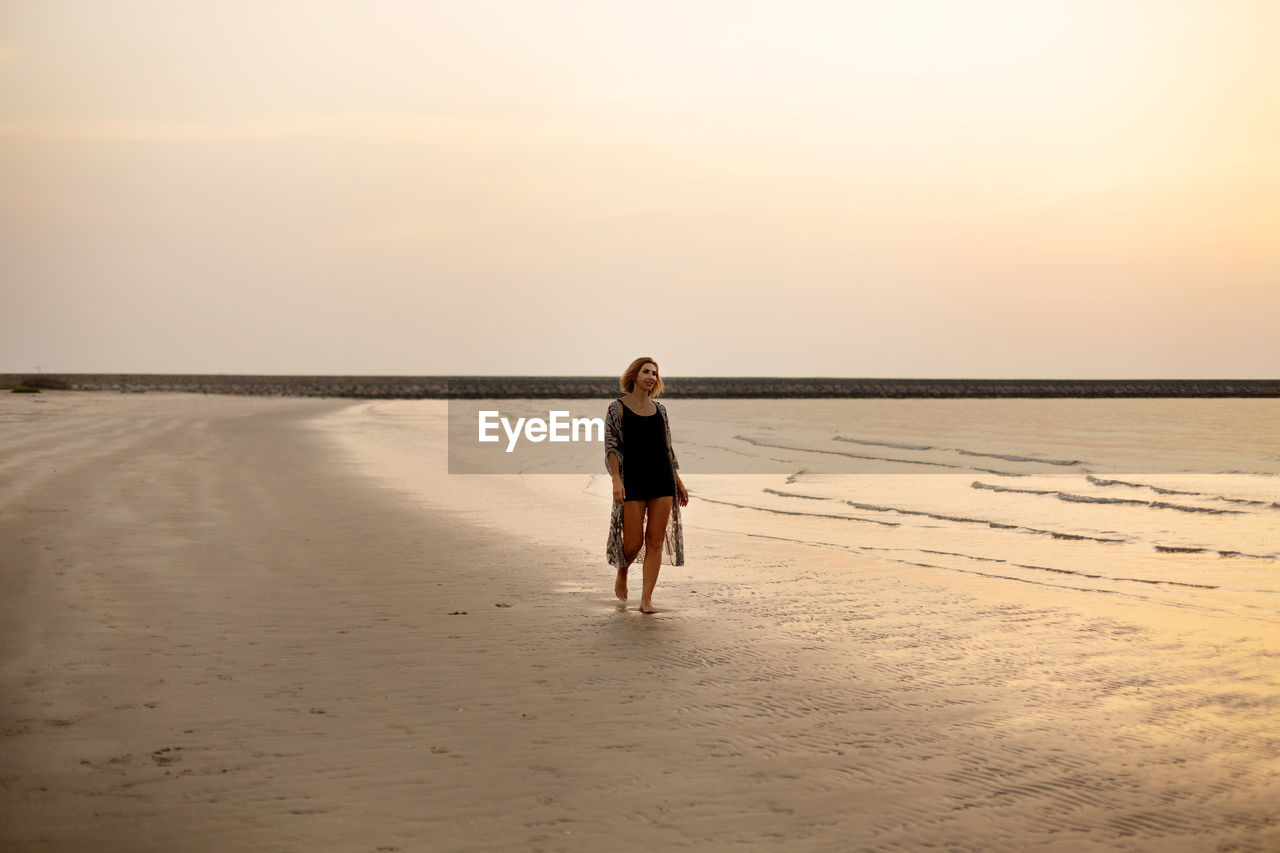 Beautiful girl strolls along the beach by the ocean at sunset