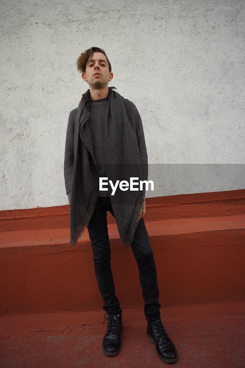 Full length portrait of young man standing against wall