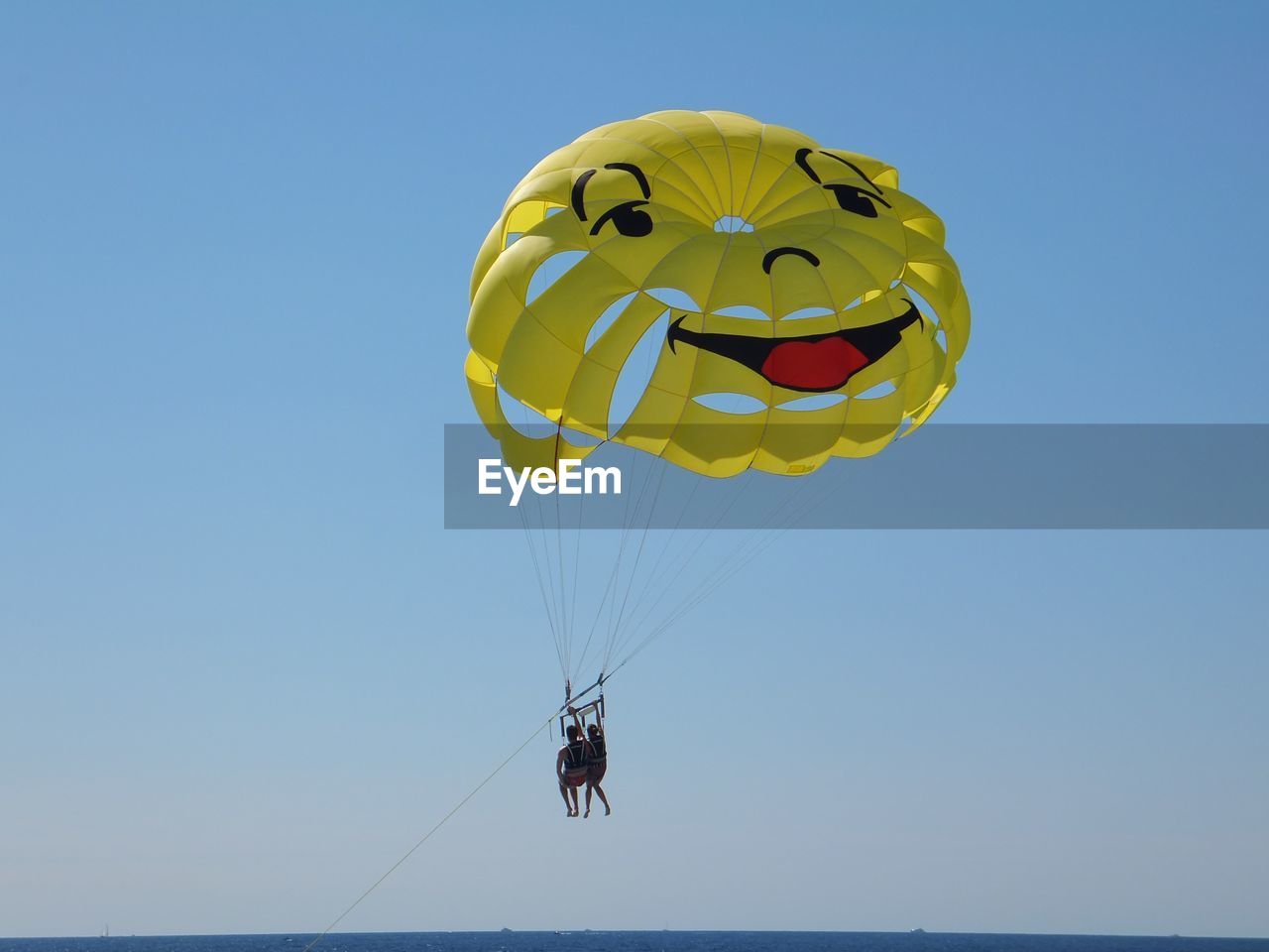 Low angle view of smiley face parachute flying against clear sky