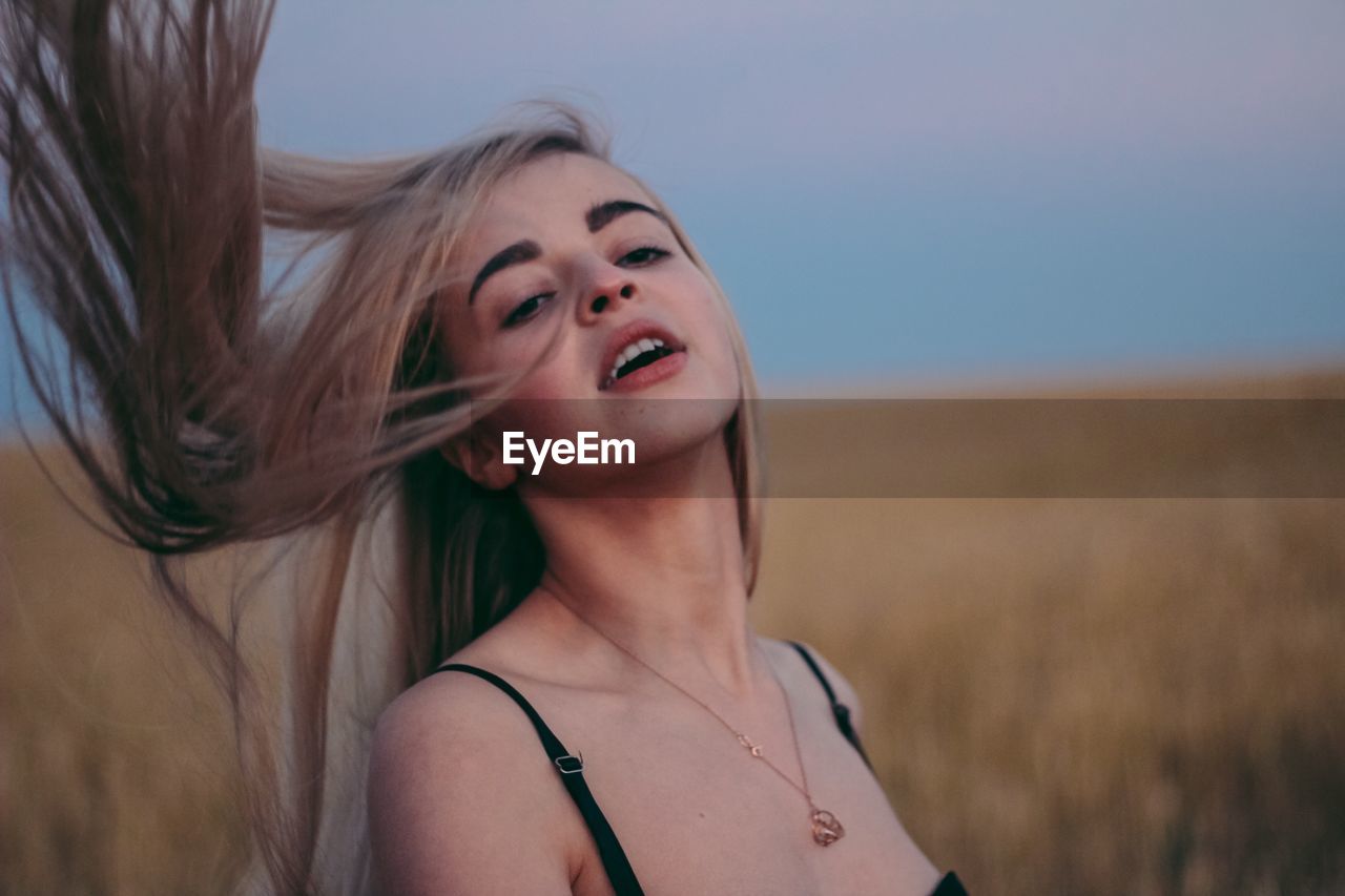 Beautiful woman tossing hair on field against sky