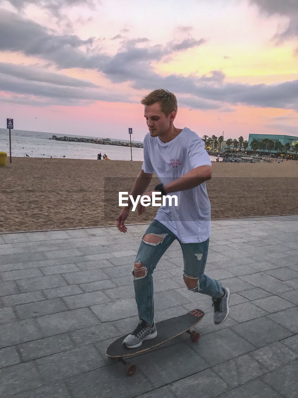 Full length of man skateboarding by beach on footpath during sunset