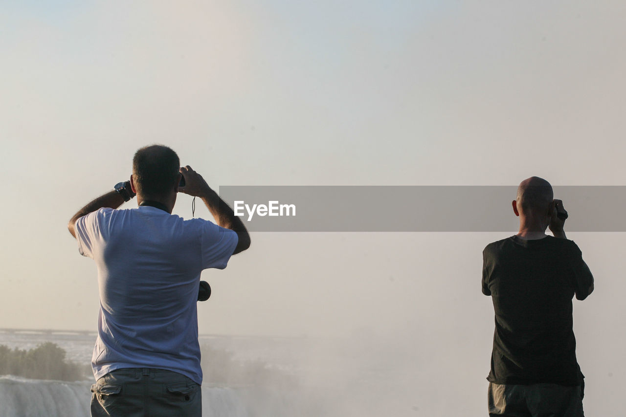 Rear view of men at niagara falls against sky