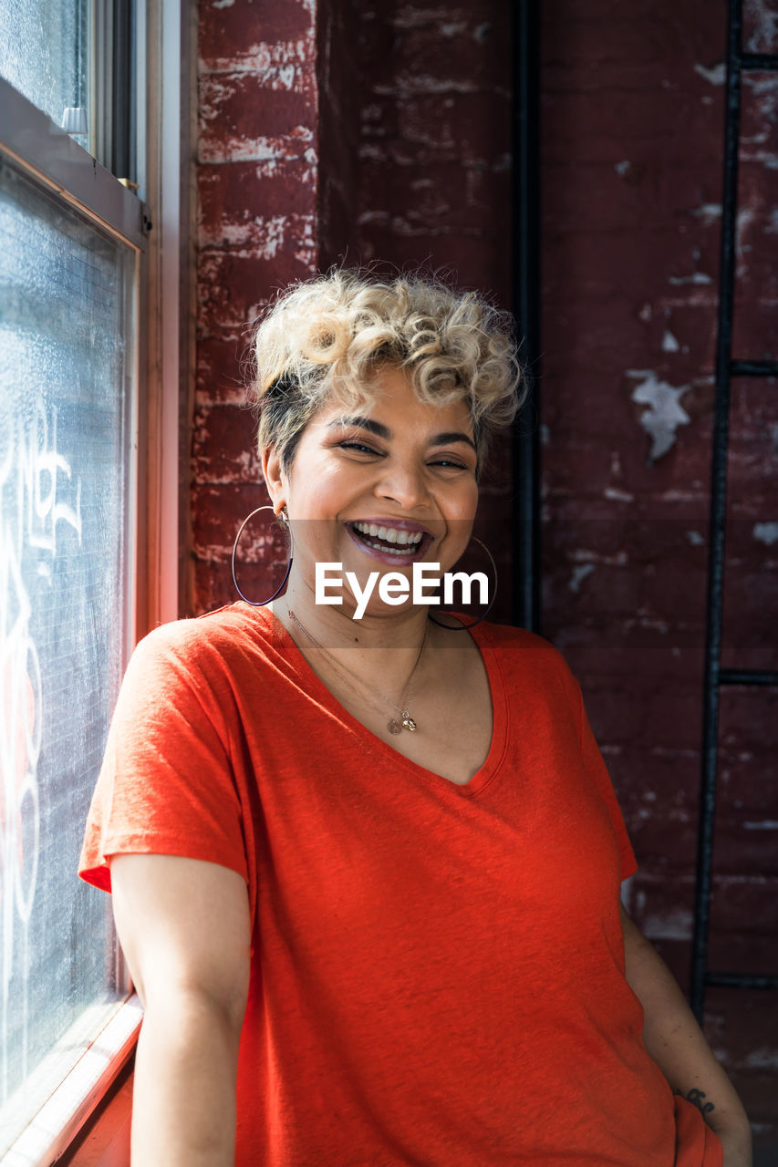 Portrait of cheerful woman with short hair standing by window at home