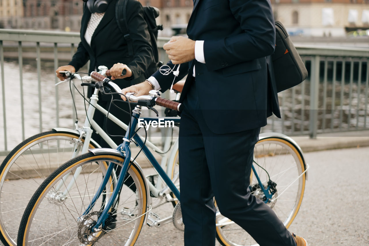 Midsection of businessman and businesswoman walking with bicycles on bridge in city