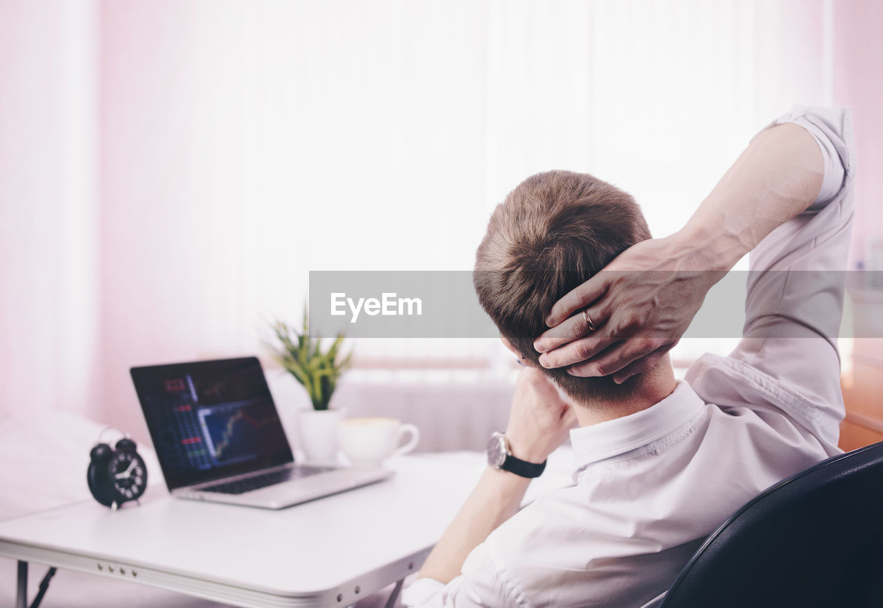 Rear view of businessman sitting by laptop on table in office