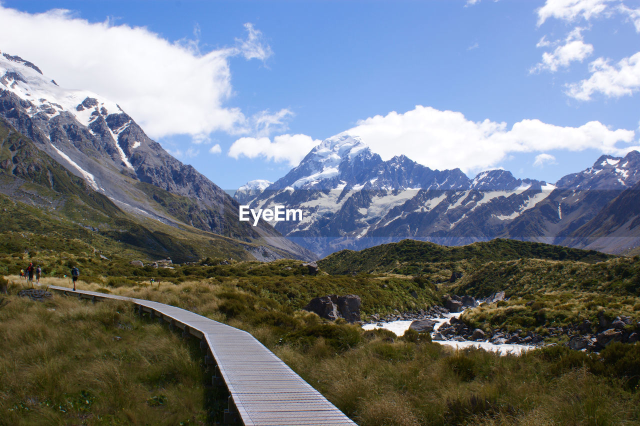 Boardwalk on grassy field by mountains against sky