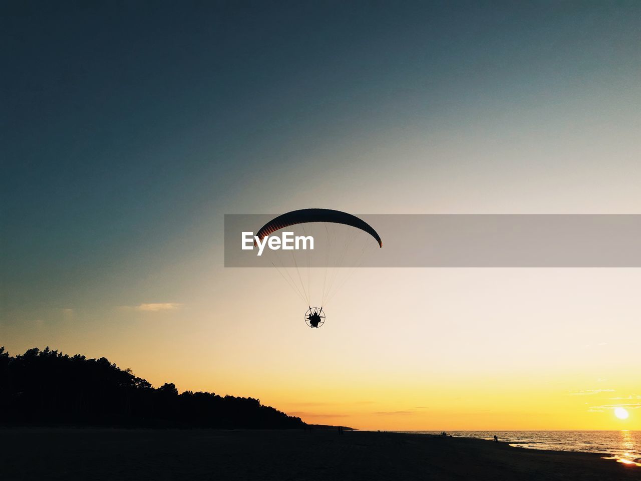 Silhouette person paragliding against sky during sunset