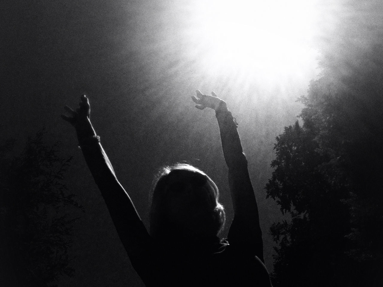 Silhouette girl with arms raised standing against sky on sunny day