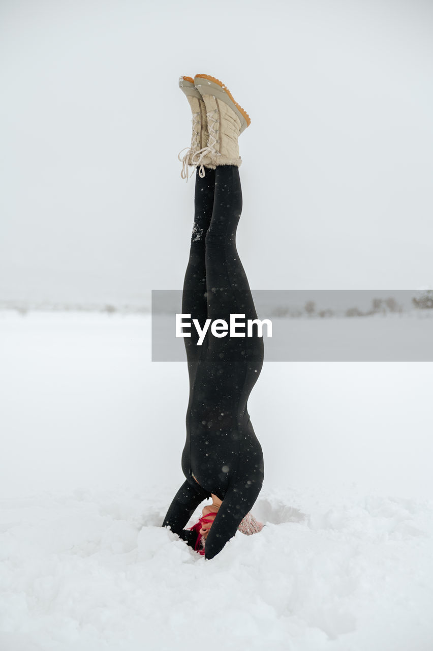 Fit female balancing in salamba shirshasana on snowy meadow while doing yoga in winter