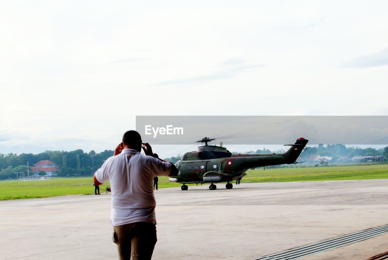 Man walking at airport runway against sky