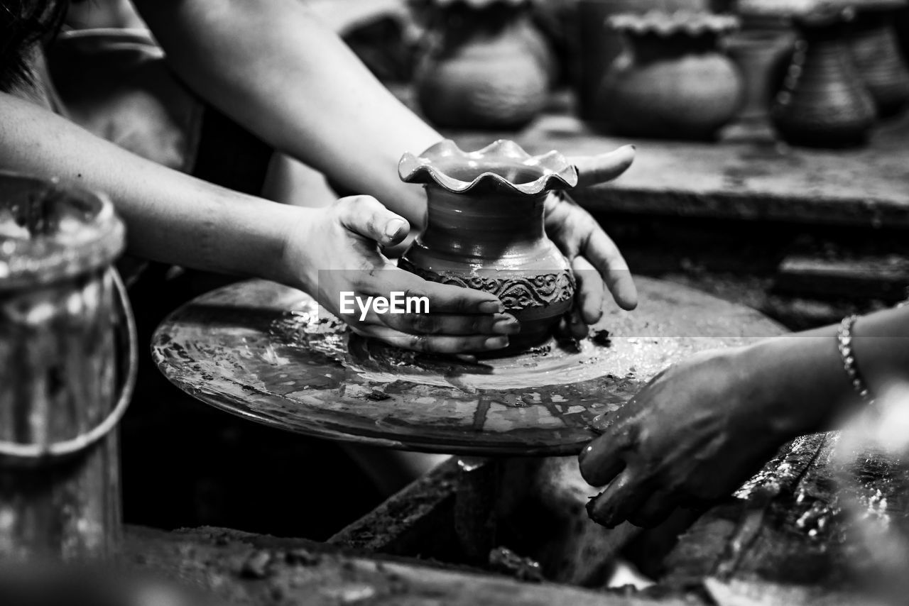 Cropped hands of people molding shape on pottery wheel