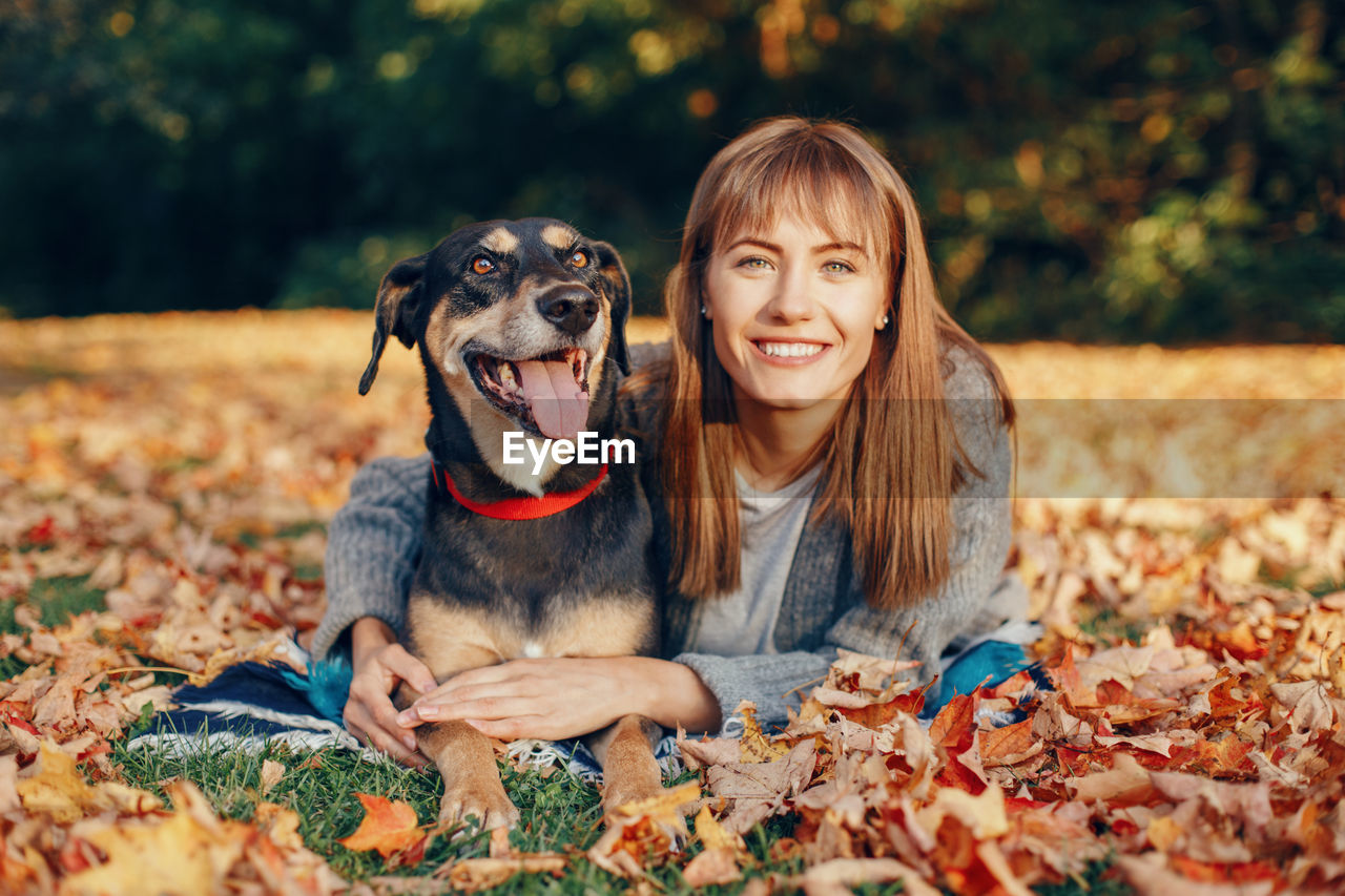 Portrait of young woman with dog lying on leaves during autumn