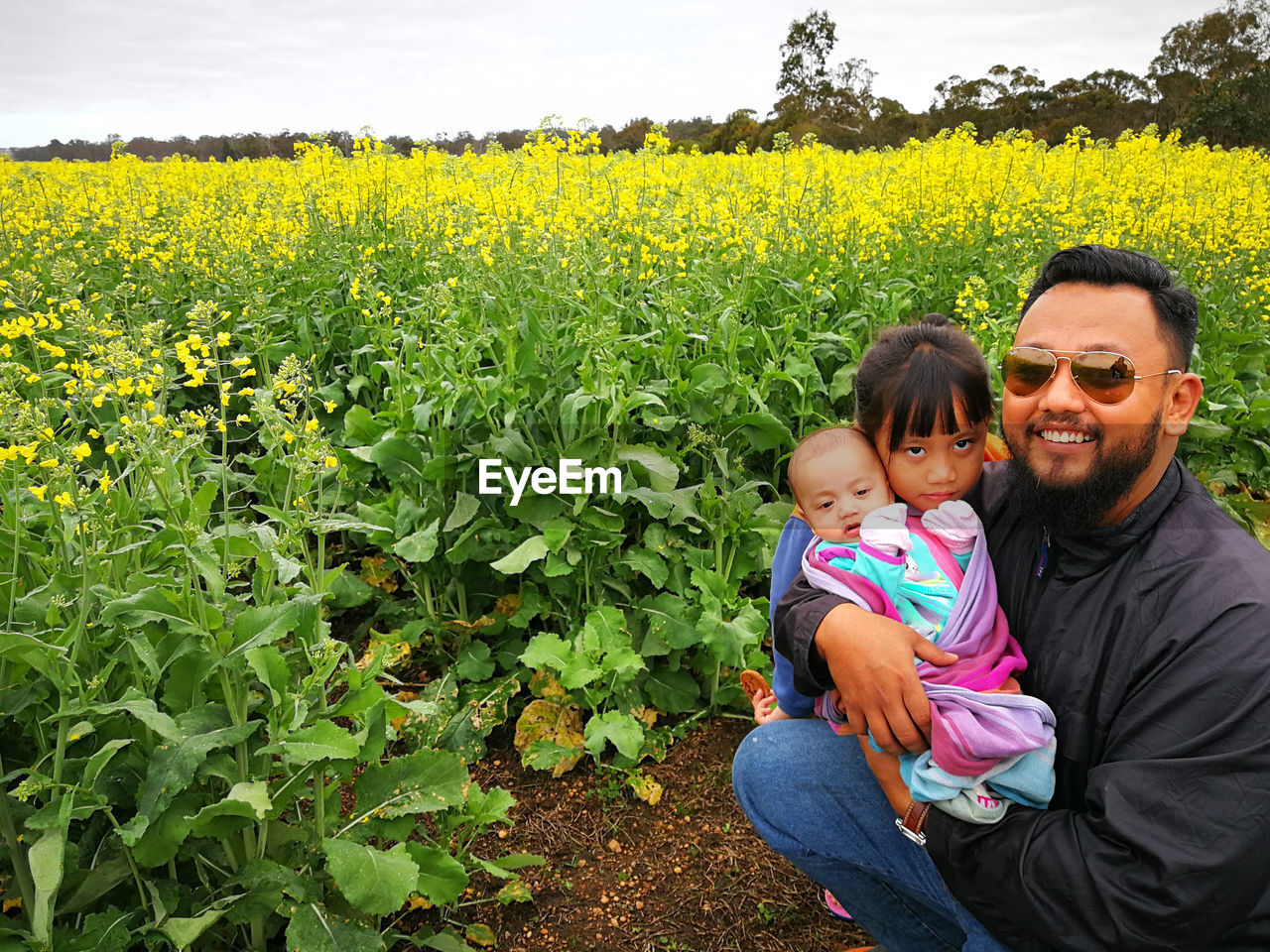 Portrait of father with daughters on field against sky