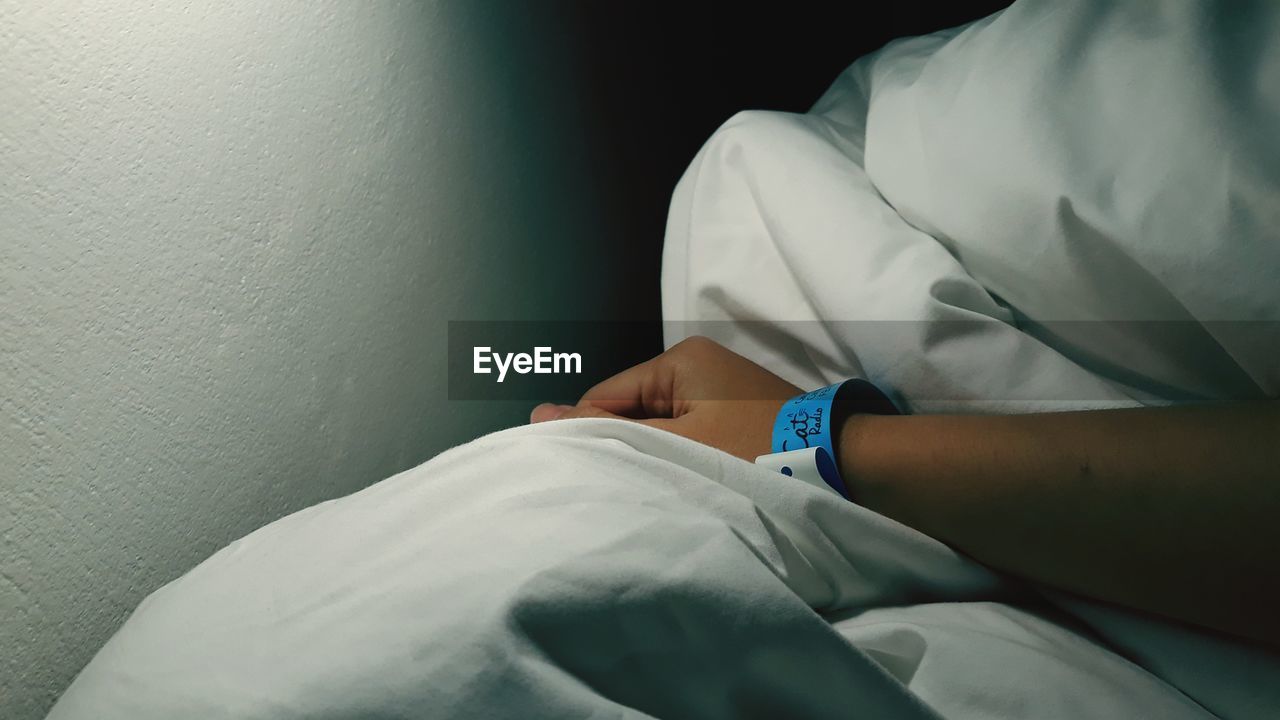 Close-up of patient wearing hospital identification bracelet on bed sheet in hospital