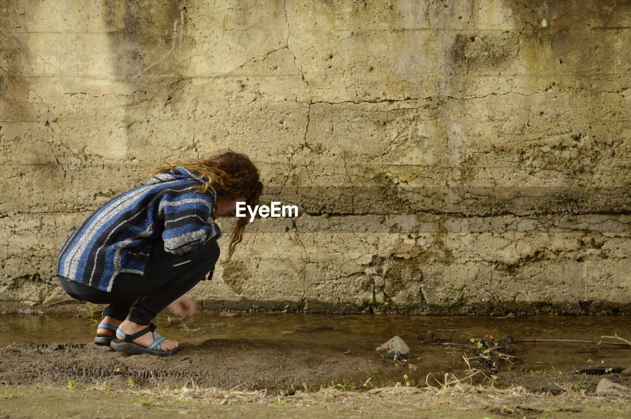 Side view of woman crouching by puddle on field