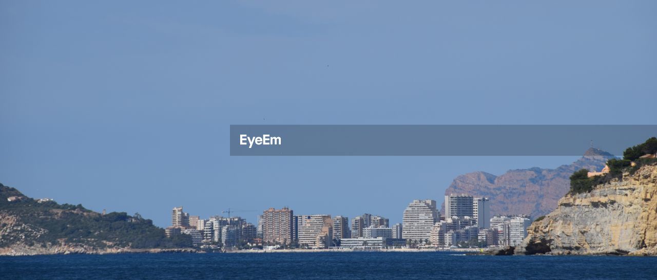 Sea by buildings against clear blue sky