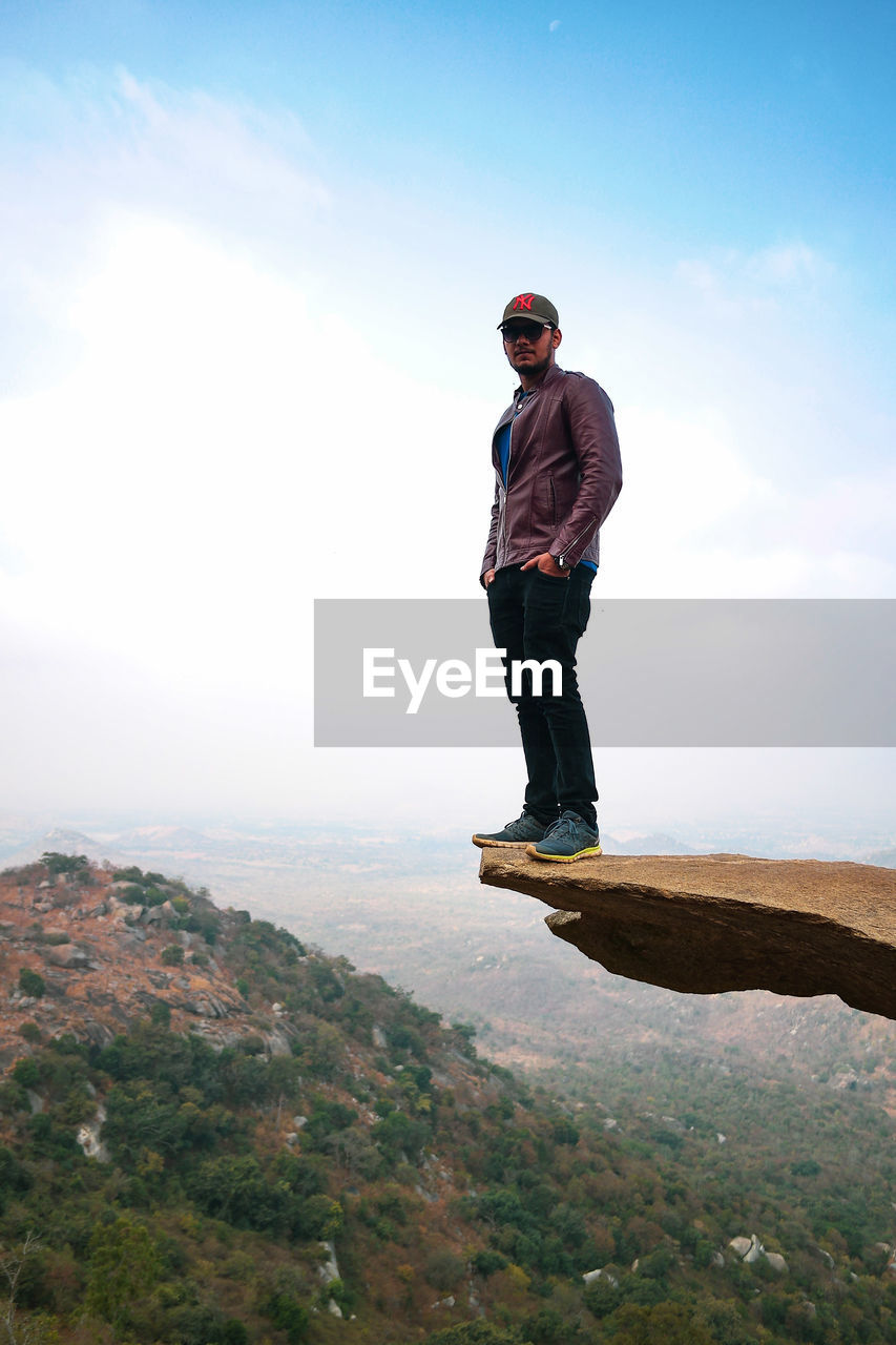 Portrait of man standing on rock formation against sky
