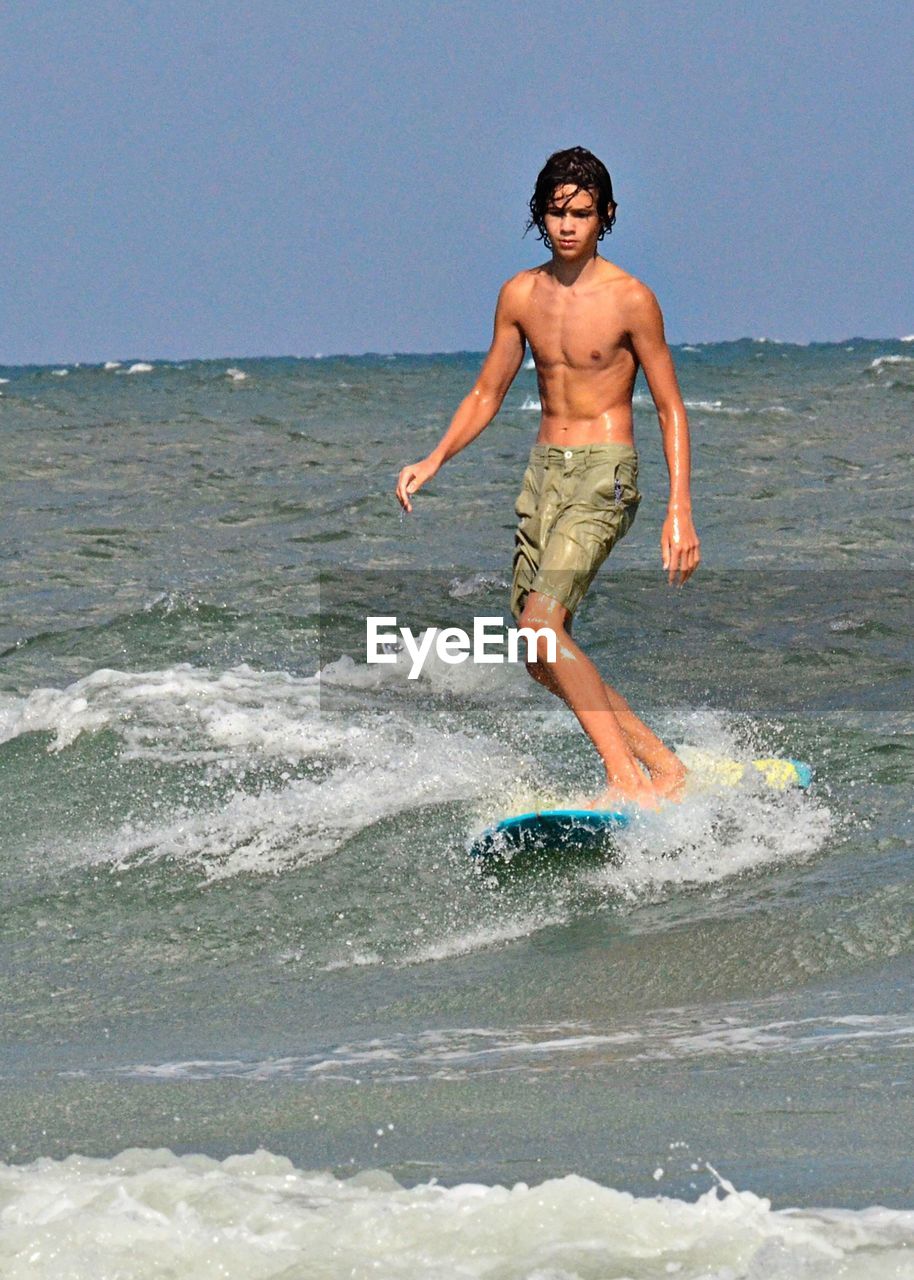 FULL LENGTH OF SHIRTLESS YOUNG MAN JUMPING ON BEACH