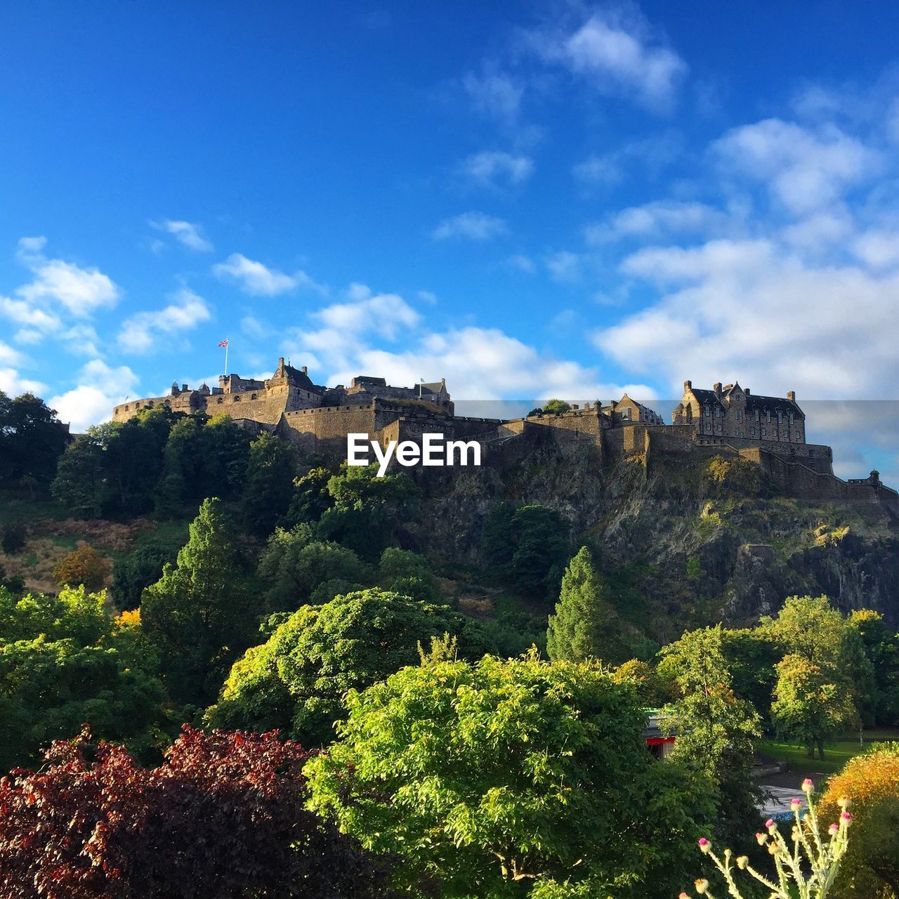 Low angle view of edinburgh castle and trees against cloudy blue sky