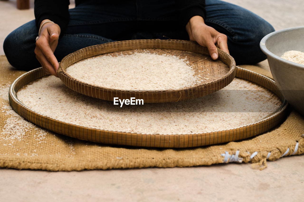 Low section of person sieving rice in wicker plate