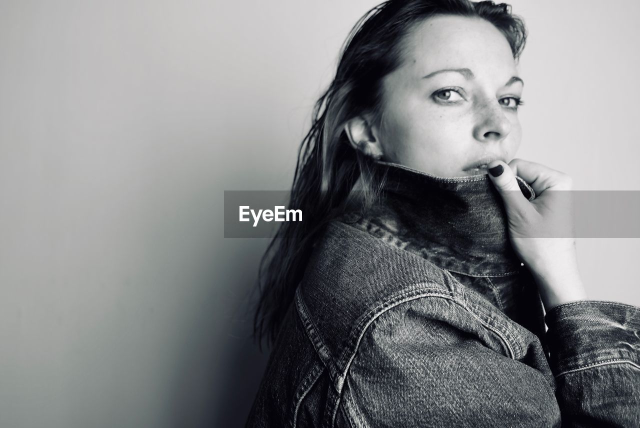 Portrait of woman wearing denim jacket against wall