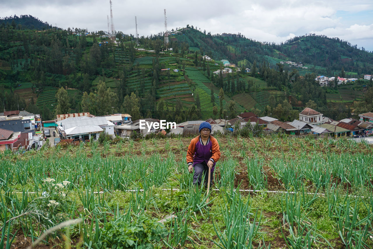 MAN WORKING ON FIELD AGAINST MOUNTAIN