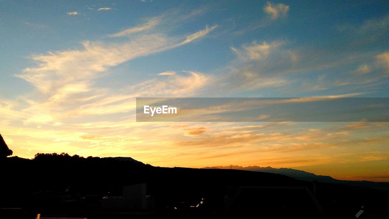 Low angle view of silhouette mountains against cloudy sky at sunset